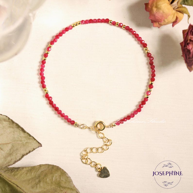 Pu&ograve; includere: Un braccialetto delicato realizzato con piccole perle di pietre preziose rosse e dettagli dorati. Il braccialetto ha una chiusura a forma di cuore.