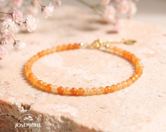 May include: A delicate bracelet featuring small, faceted orange gemstone beads arranged in a circular pattern. The jewelry piece includes a thin gold-toned metal chain with a small circular tag at the clasp. The text JOSEPHINE is visible.