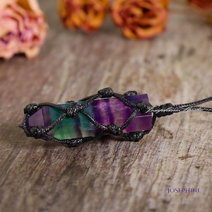 May include: A rainbow fluorite crystal point wrapped in a black macrame cord necklace. The crystal is a vibrant mix of purple, green, and blue.