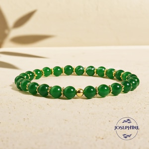 May include: A green beaded bracelet with gold accents and a single gold bead. The bracelet is made of round, polished green beads strung together with gold-coloured metal. The bracelet is a piece of jewellery.