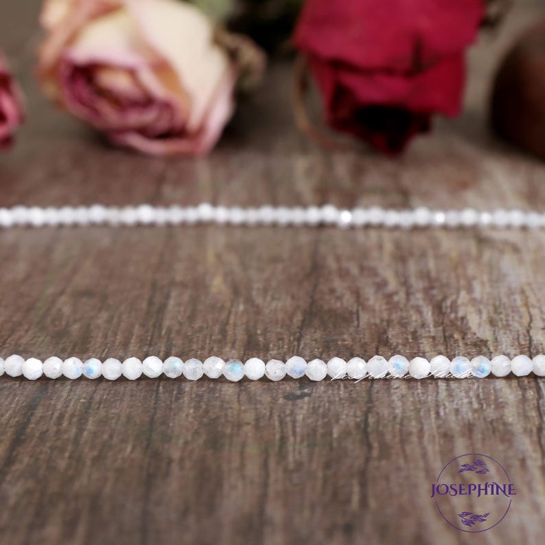 May include: A strand of white moonstone beads on a wooden surface. The beads are small and round, and they have a subtle iridescent sheen.