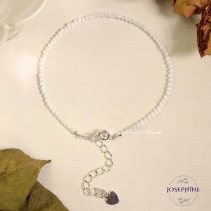 May include: A delicate white gemstone bracelet with a silver clasp and heart charm. The bracelet is made with small, round beads and has an adjustable length.