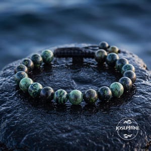 Peut inclure: Un bracelet de perles composé de pierres rondes et polies dans des tons de vert foncé, vert forêt et noir avec des motifs naturels marbrés. Les perles sont montées sur un cordon sombre avec un fermoir coulissant et le texte JOSEPHINE.