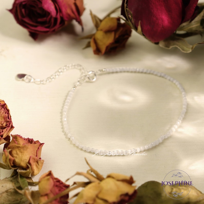 May include: A delicate silver chain bracelet with small white beads. The bracelet has a lobster clasp closure.