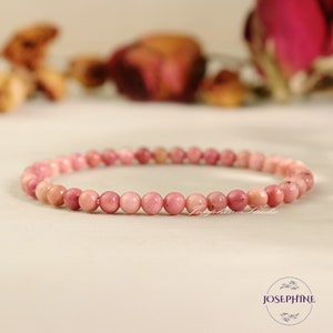 May include: A pink gemstone bracelet made of small, round beads. The bracelet is on a white surface.
