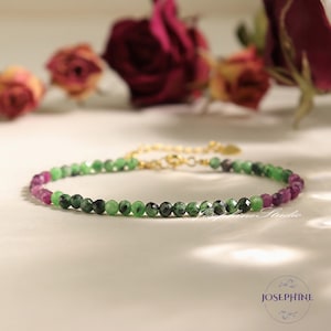May include: A delicate gold chain bracelet with green and pink gemstone beads. The bracelet features a mix of round and faceted beads.