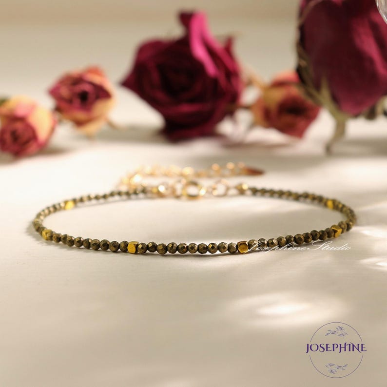 May include: A delicate gold and green beaded bracelet with a simple design. The bracelet is made of small, round beads that are strung together on a thin gold chain.