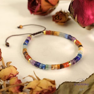 May include: A colourful beaded bracelet featuring a range of stones, including amethyst, lapis lazuli, and tiger's eye. The bracelet is adjustable with a sliding knot.