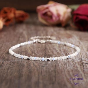May include: A delicate silver bracelet with small white moonstone beads. The bracelet is on a wooden surface.