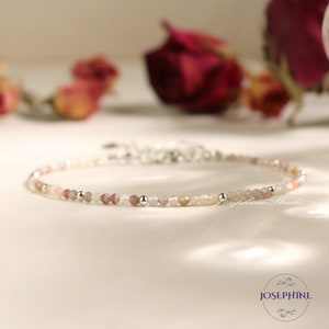 Puede incluir: Delicada pulsera de cuentas con pequeñas cuentas redondas multicolores en tonos rosa, melocotón y blanco. La pulsera tiene un cierre plateado y se muestra sobre una superficie blanca. Una joya delicada.