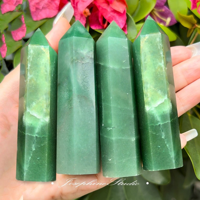 May include: Four green jade crystal points, each with a slightly different shade of green, are arranged in a row. The points are smooth and polished, and they have a natural, organic look.