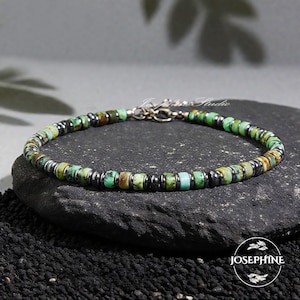 Puede incluir: Una pulsera de cuentas con cuentas de turquesa verde y marrón intercaladas con cuentas metálicas de color gris oscuro. La pulsera se muestra sobre una piedra oscura. El cierre es plateado. El nombre de la marca "Josephine" es visible.