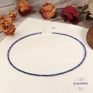 May include: A delicate necklace featuring small, faceted, deep blue beads. The necklace has a silver-colored clasp and is displayed on a white surface. The word "JOSEPHINE" is visible in the lower right corner.