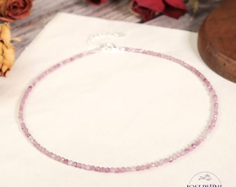 Könnte beinhalten: Eine zarte Halskette aus kleinen, facettierten rosa Edelsteinperlen, die kreisförmig angeordnet sind. Die Kette verfügt über einen silberfarbenen Metallverschluss und eine verstellbare Kettengliederverlängerung auf der Rückseite sowie ein dezentes Logo.