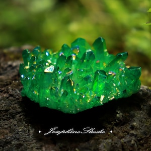 May include: A cluster of green iridescent quartz crystals with a rainbow sheen. The crystals are arranged in a cluster and have a rough, natural texture.