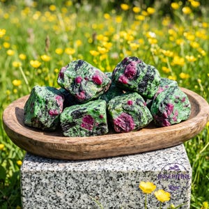 May include: A collection of raw ruby in zoisite mineral stones featuring vibrant magenta-pink ruby crystals embedded within a matrix of mottled green zoisite and black hornblende, arranged in a shallow, oval-shaped wooden bowl.