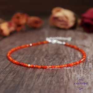 May include: A delicate bracelet composed of small, faceted orange carnelian beads. The bracelet features a silver-toned metal clasp and an adjustable chain extension. The text "Josephine Studio" is visible in white script near the center.
