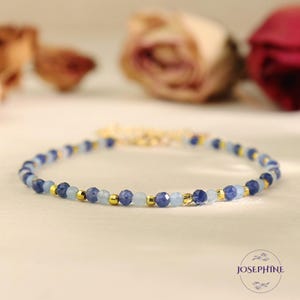 Op de afbeelding: Een delicate gouden kettingarmband met afwisselende blauwe en lichtblauwe edelsteen kralen.