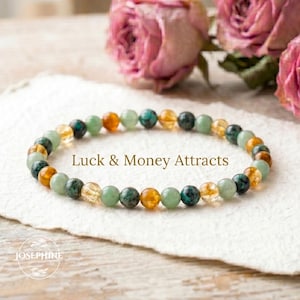 May include: A beaded bracelet with a mix of green, yellow, and orange gemstones. The bracelet is displayed on a white surface with the text "Luck & Money Attracts". Pink roses are in the background.