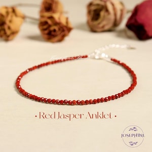 May include: Red jasper anklet with a silver clasp. The anklet is made of small, round beads and is about 9 inches long. The anklet is on a white background with a few dried roses.