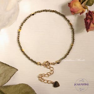 May include: A gold chain bracelet with a heart charm and a clasp. The bracelet is made of small, dark green beads.