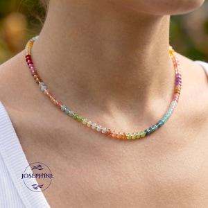 May include: A beaded necklace featuring a sequence of small, multi-coloured gemstone rondelles in shades of pink, blue, green, yellow, and orange, interspersed with tiny gold-toned metal spacer beads along the entire length of the strand.