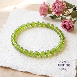 May include: A circular bracelet composed of small, smooth, translucent light green peridot beads arranged in a continuous loop. The beads have a polished finish and a consistent round shape, creating a uniform appearance throughout the jewelry piece.