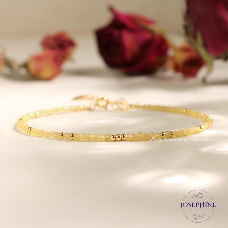 May include: A delicate bracelet featuring small, faceted pale yellow beads interspersed with polished gold-tone metal spheres. The jewelry piece includes a gold-tone metal clasp and chain extender. The text Josephine Studio is visible.