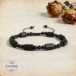 May include: Black beaded bracelet featuring rectangular and round beads. The bracelet has a sliding knot closure for adjustable sizing. The beads are a mix of smooth and textured surfaces. The bracelet is displayed on a neutral background.