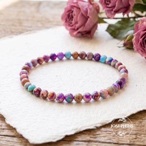 Könnte beinhalten: Ein Perlenarmband aus kleinen, runden, polierten Steinen in einer abwechslungsreichen Farbpalette aus Violett, Türkis, Blau und Hellbraun. Die Perlen sind in einem durchgehenden kreisförmigen Muster angeordnet und zeigen natürliche Maserungen.