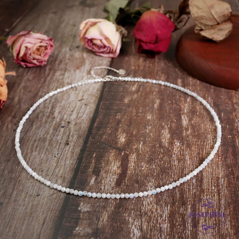 May include: A delicate white moonstone necklace with small, round beads. The necklace is on a wooden surface.