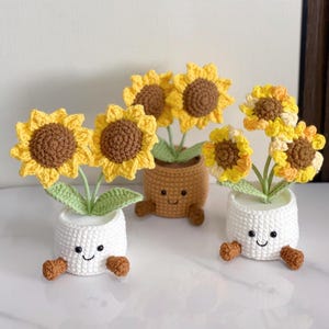 Può includere: Girasoli all'uncinetto in vasi sorridenti. I girasoli hanno petali gialli e centri marroni. I vasi sono bianchi e marroni, con facce sorridenti e piedini. Un'allegra decorazione per la casa fatta a mano.