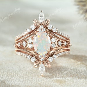 May include: A rose gold ring featuring an oval opal gemstone surrounded by smaller diamonds. The ring has a delicate, intricate design with floral motifs and a pointed crown.