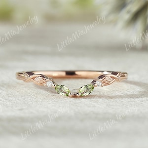 May include: Rose gold ring with a leaf design. The ring features two green marquise-cut gemstones and small white gemstones. The band curves in a V-shape. The words "Little Mia Jewelry" are printed on the image.