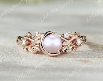 May include: A rose gold ring with a delicate leaf design and a single pearl in the center. The ring is set with small diamonds on each side of the pearl.