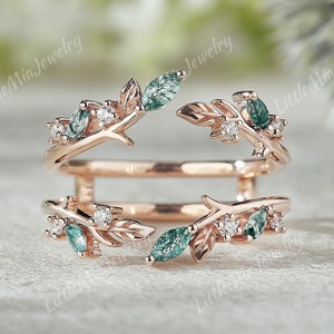 Puede incluir: Un delicado anillo de oro rosa con un diseño de doble banda. El anillo presenta un diseño de rama frondosa con piedras verdes y blancas.