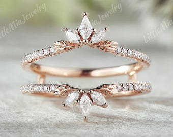 May include: A rose gold ring guard featuring two bands connected by vertical bars. Each band is adorned with small pavé-set stones and a central cluster of marquise-cut stones arranged in a leaf-like pattern. The text LittleMiaJewelry is visible.
