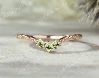 May include: A delicate rose gold ring with a v-shaped band adorned with three small green gemstones.