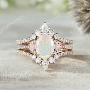 May include: A three-piece rose gold engagement ring set featuring a large oval opal center stone surrounded by smaller diamonds. The band is adorned with delicate pave diamonds and two smaller pink opal accent stones.