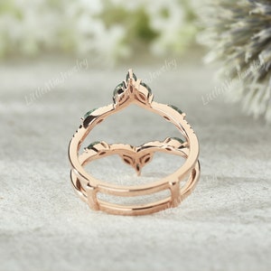 May include: A rose gold ring with a delicate, open design featuring a row of green gemstones. The ring is designed to be worn as a wedding band or engagement ring enhancer.
