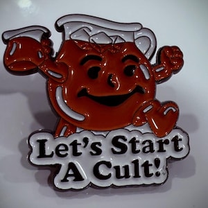 May include: A red and white enamel pin featuring a cartoon pitcher of orange juice with a smiling face and the text "Let's Start A Cult!"
