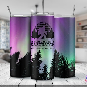 May include: A stainless steel tumbler with a purple and green aurora borealis design. The tumbler features a silhouette of Bigfoot walking with the text "Sometimes Bigfoot is confused with Sasquatch. Yeti never complain."