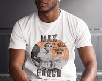 May include: White t-shirt featuring a black and white image of Max Roach playing drums at the Newport Jazz Festival in 1964. The text "Max Roach" is printed in large black letters above the image and "Newport Jazz Festival" is printed in smaller black letters below the image.