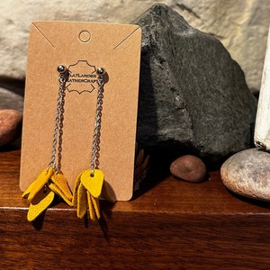 May include: A pair of yellow leather earrings with a chain and a brown card with the text "Flatlander Leathercraft".