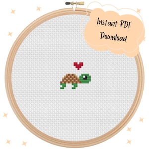 May include: A cross-stitch pattern featuring a green turtle with a brown shell and a red heart above it. The pattern is displayed in a wooden embroidery hoop.