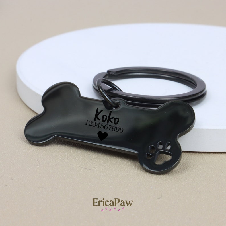 Op de afbeelding: Zwarte, botvormige hondenhanger met de naam "Koko" en het telefoonnummer "1234567890" erop gegraveerd. De hanger heeft een klein hartje en een pootprint.
