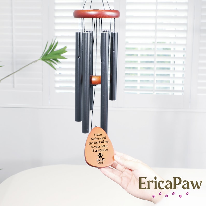 May include: Black metal wind chime with a wooden top and a brown wooden tag that reads "Listen to the wind and think of me. In your heart, I'll always be. BAILEY 2023"
