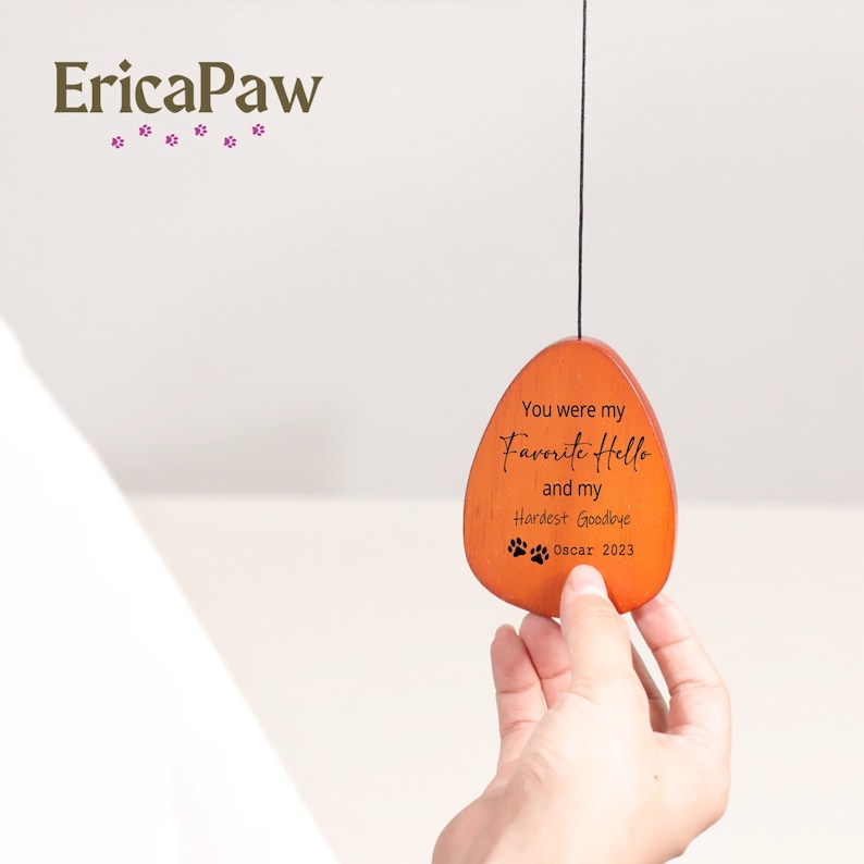 May include: A wooden heart-shaped ornament with the text "You were my Favorite Hello and my Hardest Goodbye" and "Oscar 2023" engraved on it.  The ornament is hanging from a string and has a paw print design.