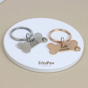 Op de afbeelding: Twee hondenpenning-sleutelhangers in de vorm van een bot met gegraveerde tekst. De sleutelhanger links is zilver en zegt "Koko Niet voeren 1234567890". De sleutelhanger rechts is goud en zegt "Koko 1234567890". Beide sleutelhangers hebben een uitsparing in de vorm van een poot.