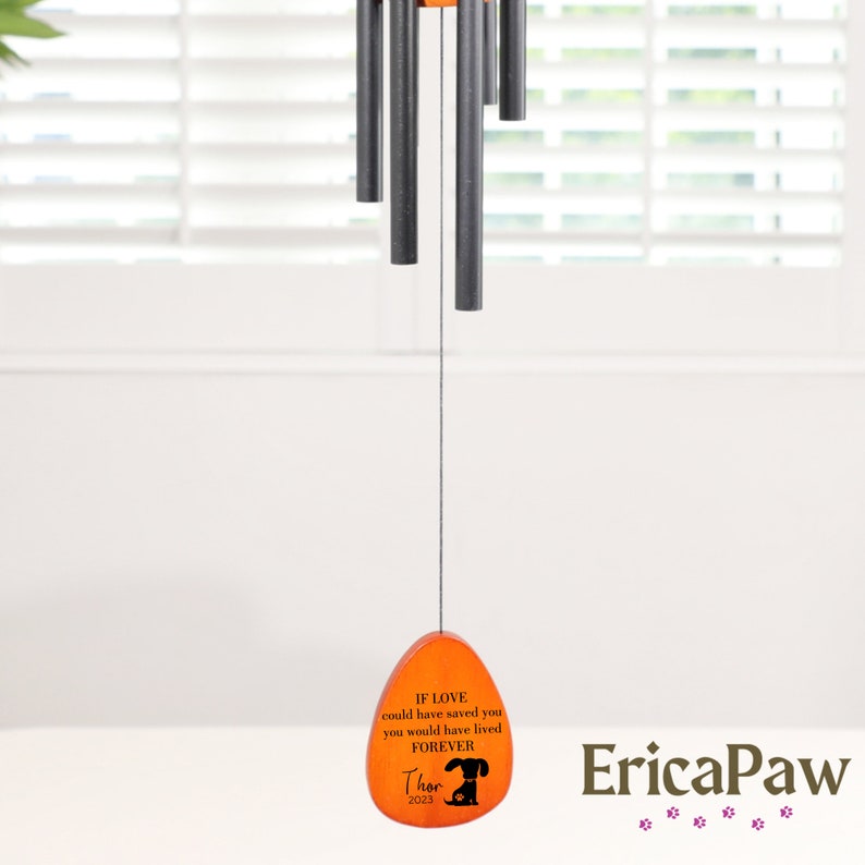 May include: Orange wooden heart-shaped wind chime with black metal tubes and a black paw print. The heart has the text "If love could have saved you, you would have lived forever. Thor 2023" and the brand name "EricaPaw" is printed below the heart.